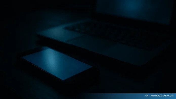 Operazione Militia: smartphone e laptop al buio, luce bluastra da schermo — metafora della propaganda neonazista online